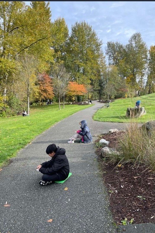 children sitting individually on the ground along a trail in a park