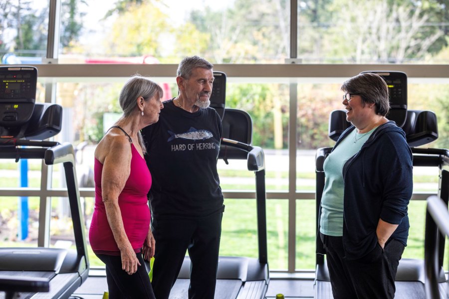Three people talking in front of treadmills.