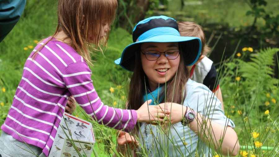 A young girl and a woman looking at an insect. 